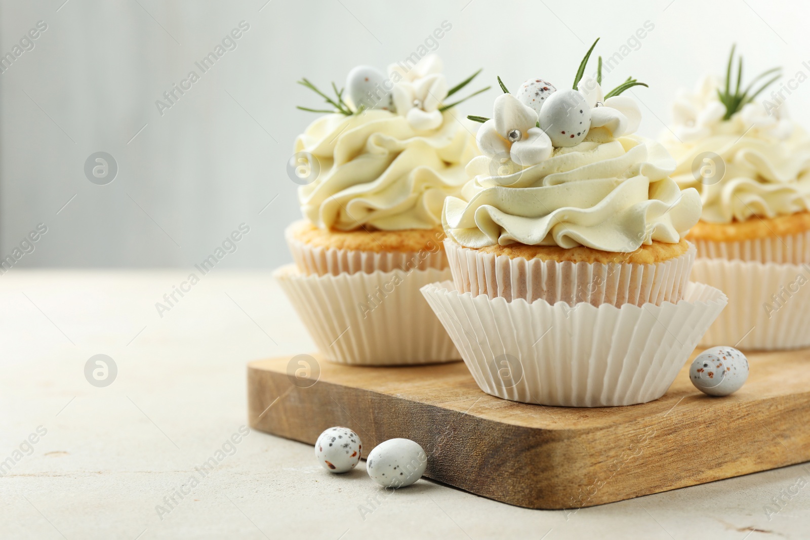 Photo of Tasty Easter cupcakes with vanilla cream and candies on gray table, space for text