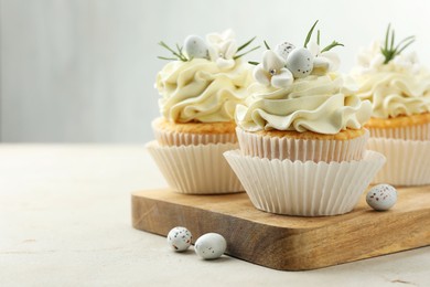 Tasty Easter cupcakes with vanilla cream and candies on gray table, space for text