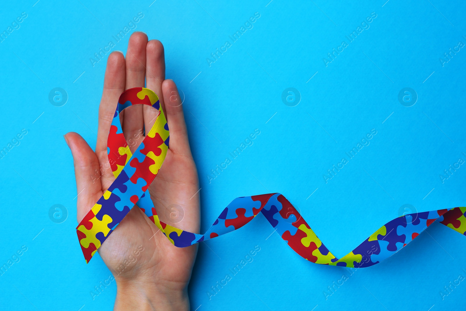 Image of World Autism Awareness Day. Woman with colorful puzzle ribbon on turquoise background, top view