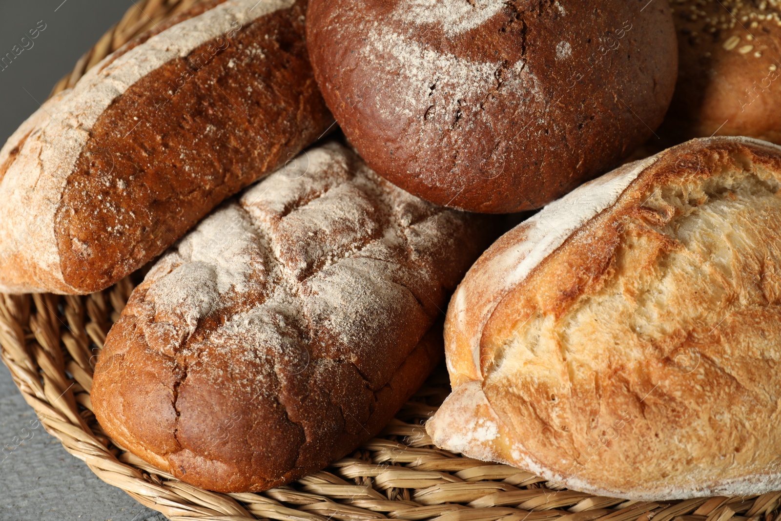 Photo of Wicker basket with different types of fresh bread on grey table, closeup