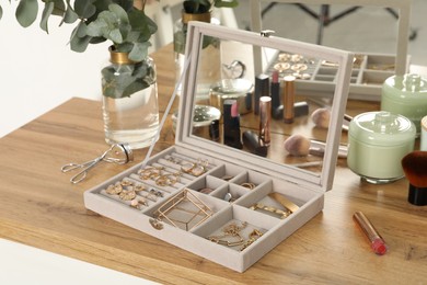 Elegant jewelry box with beautiful bijouterie, cosmetics and candles on wooden table