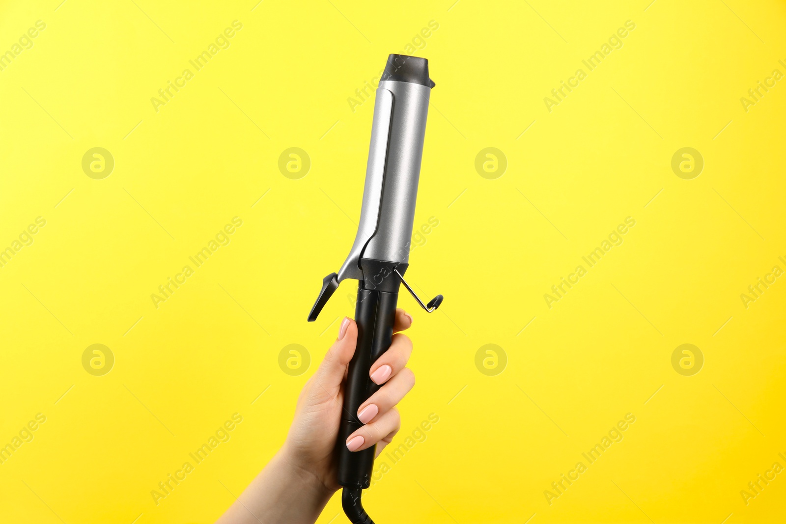 Photo of Hair styling appliance. Woman holding curling iron on yellow background, closeup