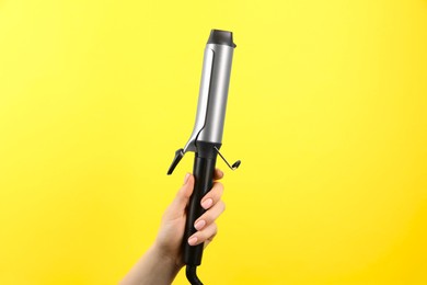 Photo of Hair styling appliance. Woman holding curling iron on yellow background, closeup