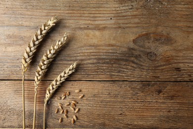 Photo of Ears of wheat on wooden table, flat lay. Space for text