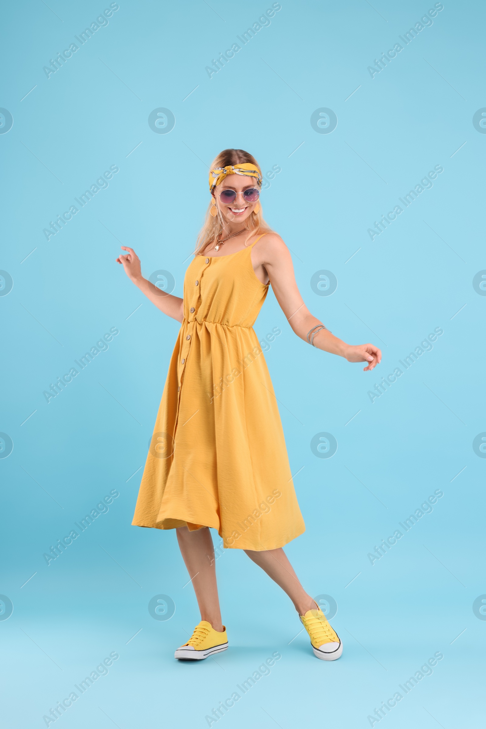 Photo of Portrait of smiling hippie woman dancing on light blue background