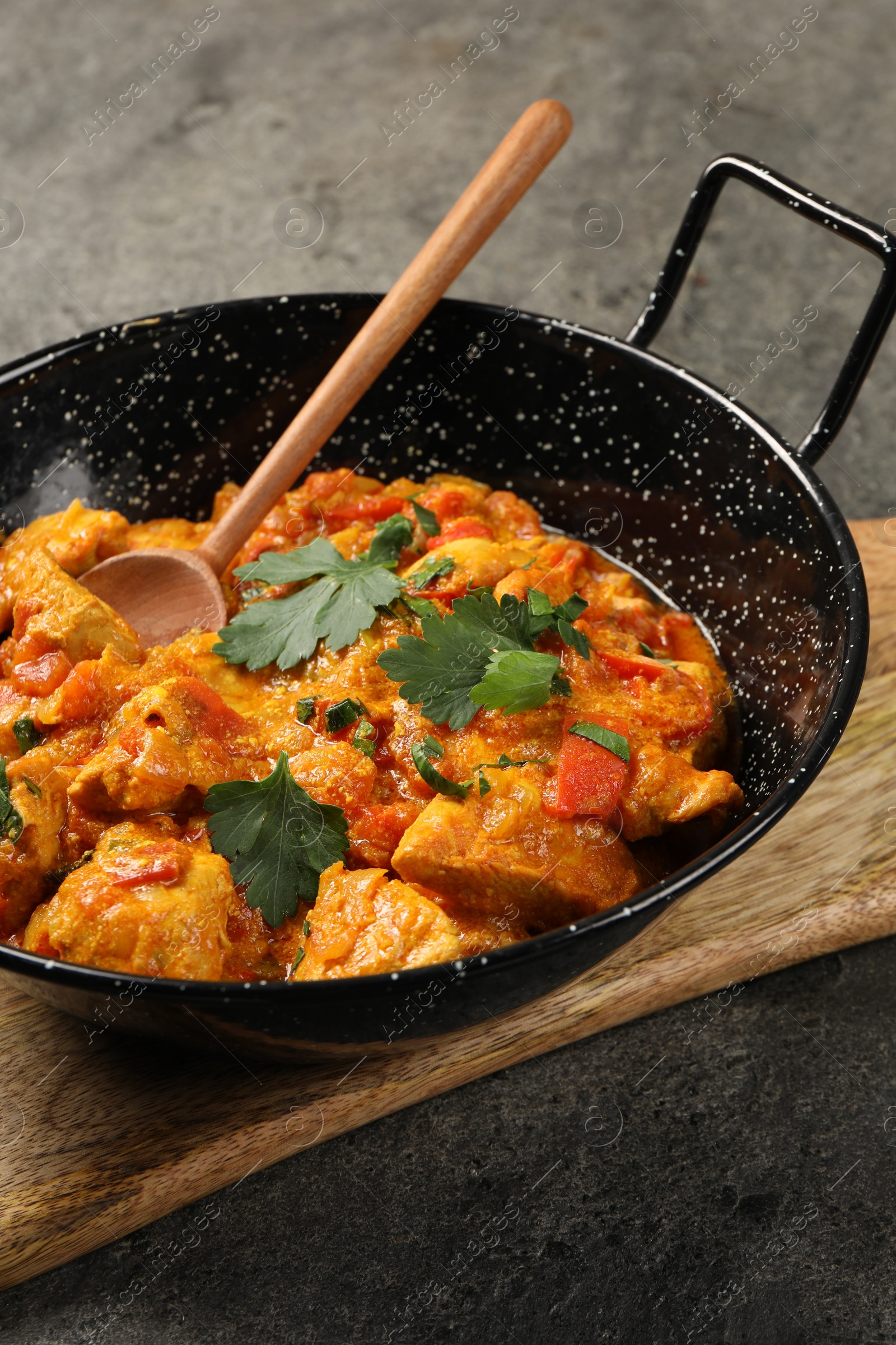 Photo of Delicious chicken curry in frying pan and spoon on grey table