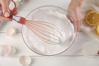 Photo of Woman making whipped cream with whisk at white wooden table, above view