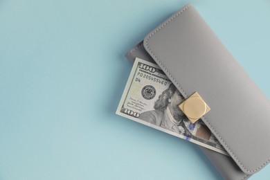 Photo of Stylish leather purse with dollar banknote on light blue background, top view. Space for text