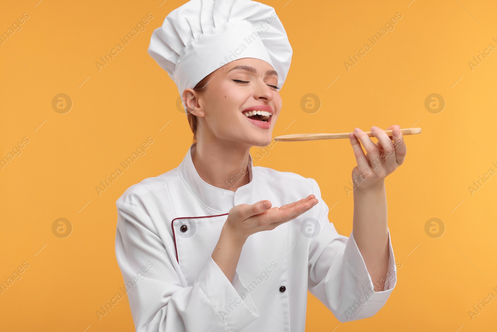 Photo of Happy chef in uniform tasting something on orange background