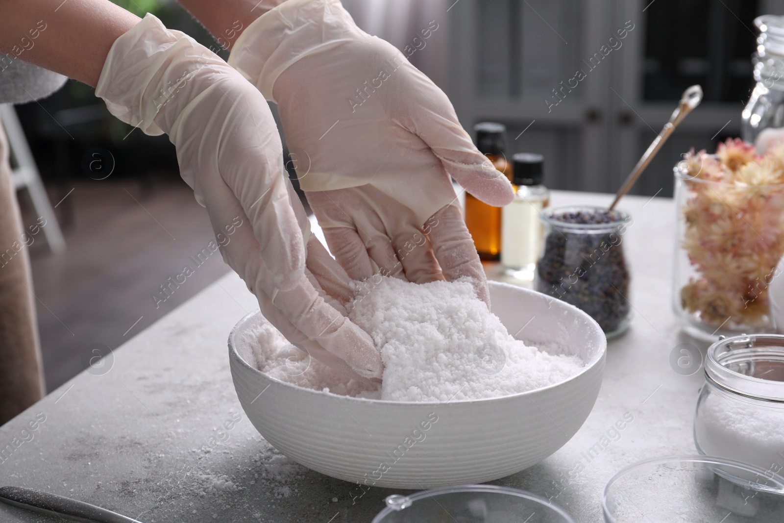 Photo of Woman in gloves making bath bomb mixture at grey table, closeup