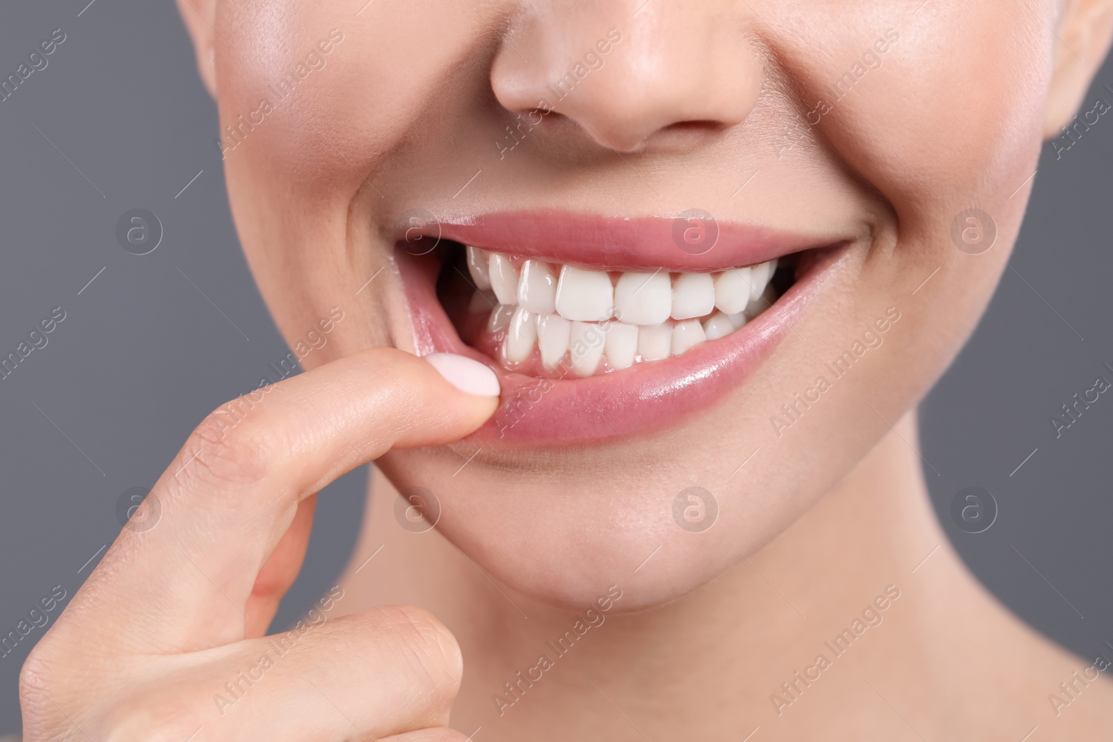 Photo of Young woman showing healthy gums on grey background, closeup