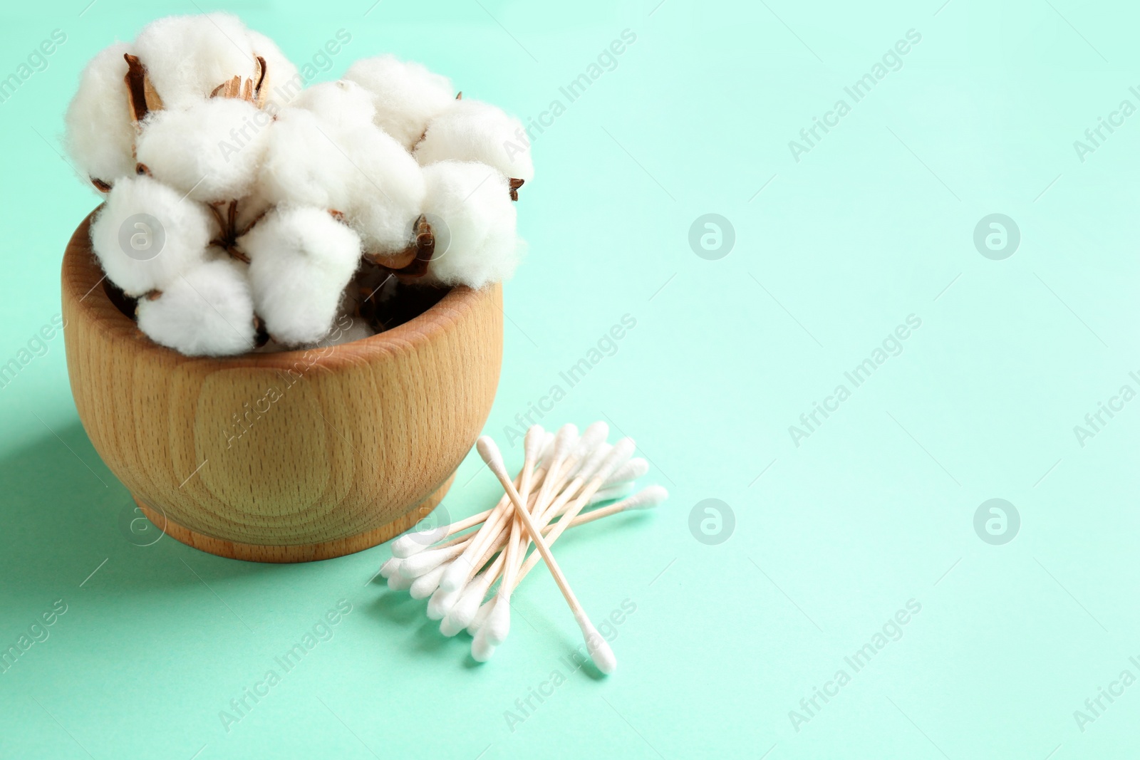 Photo of Cotton swabs and bowl of flowers on color background. Space for text