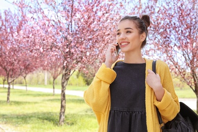 Photo of Young woman talking by phone outdoors on sunny day