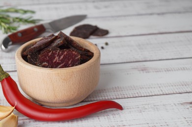 Photo of Slices of delicious beef jerky and chili on white wooden table, closeup. Space for text
