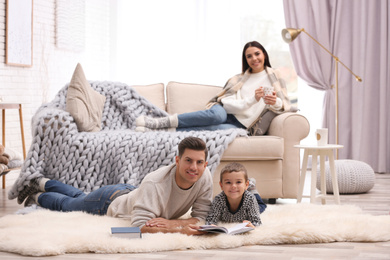 Photo of Father and his son reading books while mother resting on sofa at home. Winter vacation