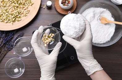 Photo of Woman in gloves making bath bomb at wooden table, top view