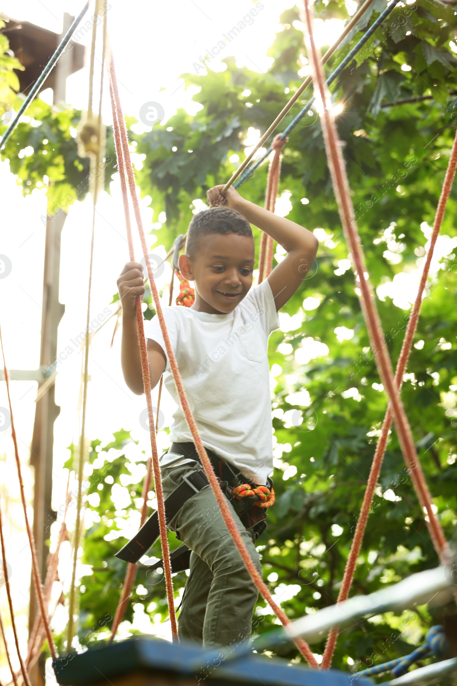 Photo of Little African-American boy climbing in adventure park. Summer camp