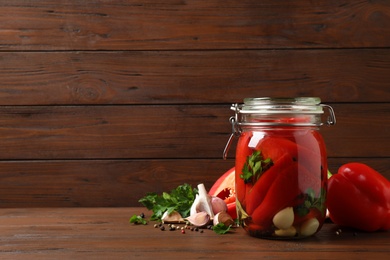 Photo of Glass jar with pickled peppers on wooden table. Space for text