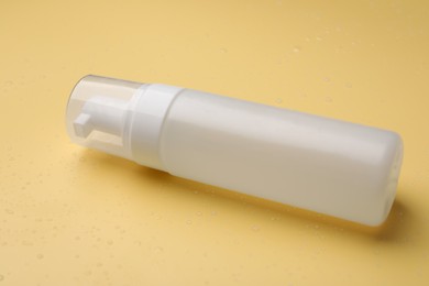 Photo of Wet bottle of face cleansing product on pale orange background