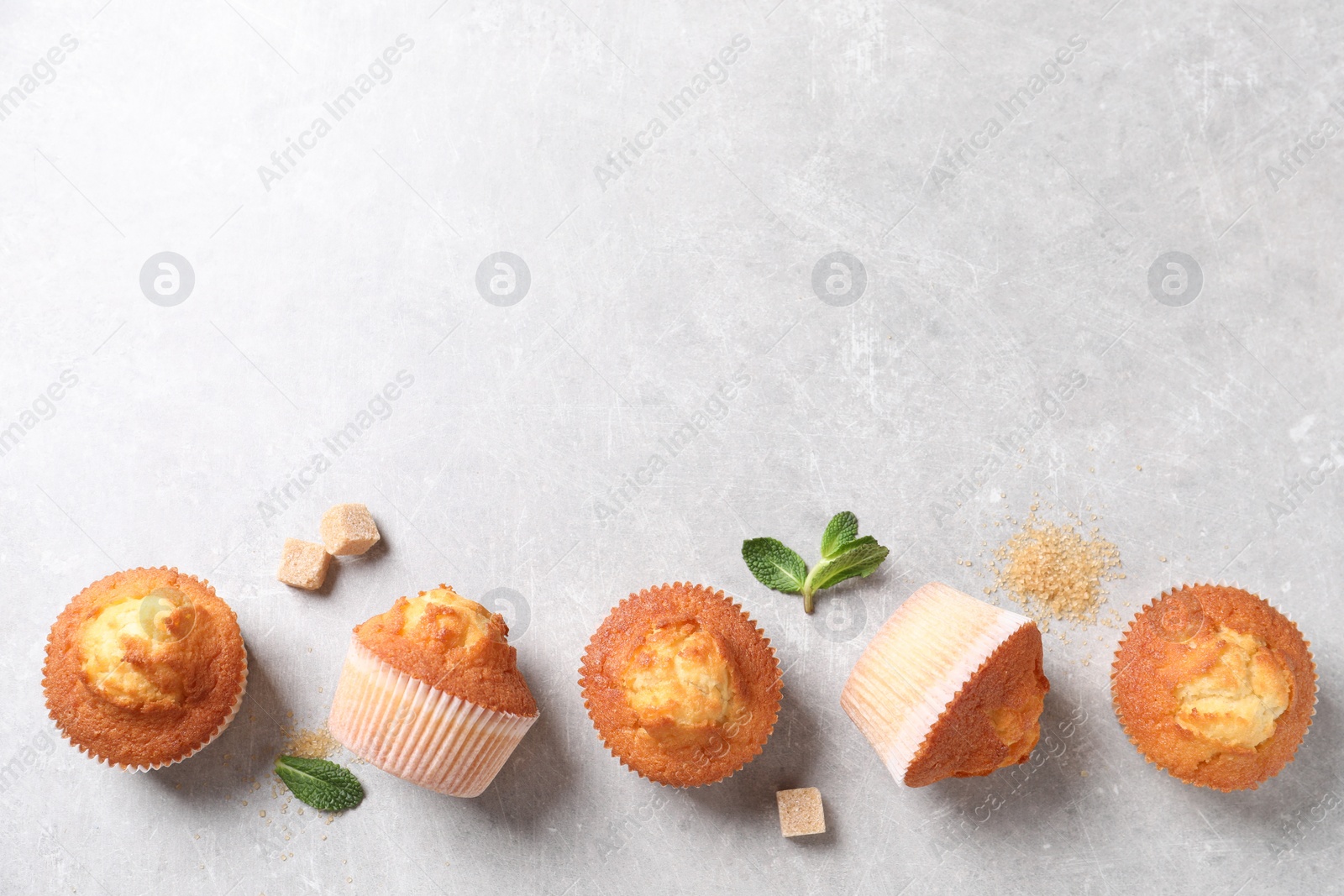 Photo of Delicious sweet muffins and brown sugar on light grey textured table, flat lay. Space for text