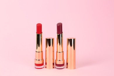 Photo of Bright lipsticks in gold tubes on pink background