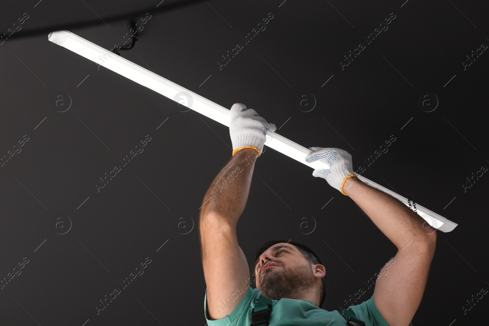 Photo of Ceiling light. Electrician installing led linear lamp indoors, low angle view