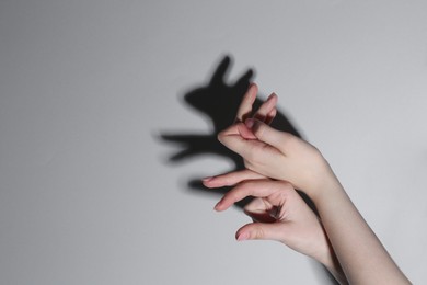 Photo of Shadow puppet. Woman making hand gesture like rabbit on grey background, closeup. Space for text
