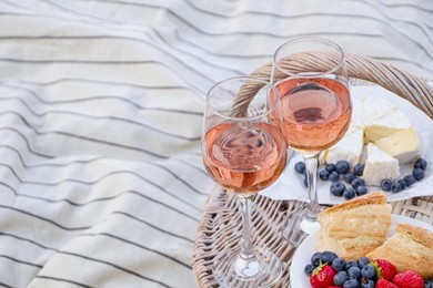 Photo of Glasses of delicious rose wine, food and basket on white picnic blanket, space for text
