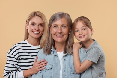 Photo of Three generations. Happy grandmother, her daughter and granddaughter on beige background
