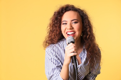 Portrait of curly African-American woman singing in microphone on color background. Space for text