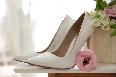 Photo of Pair of white high heel shoes, flowers and blurred wedding dress on background, space for text