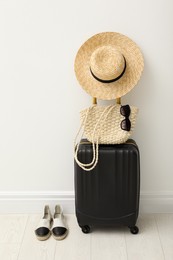 Suitcase packed for trip, shoes and summer accessories near white wall indoors