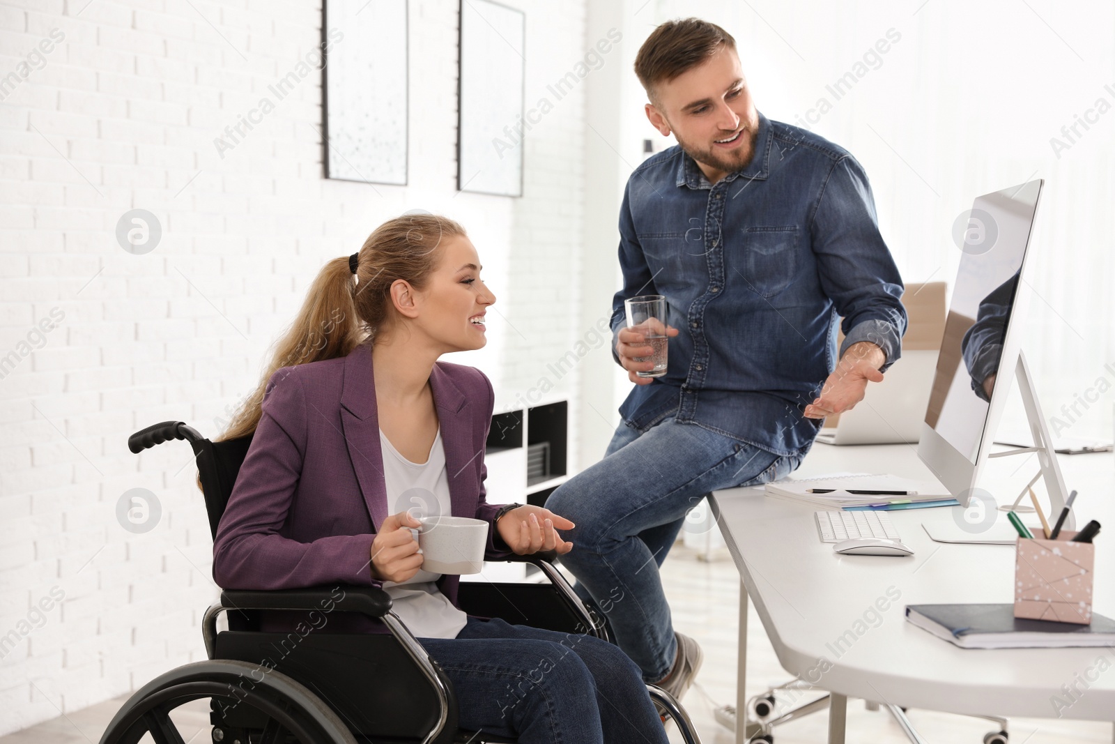 Photo of Woman in wheelchair with her colleague at workplace