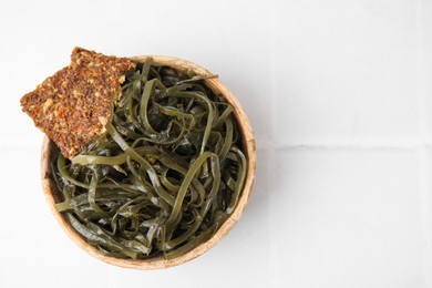 Photo of Tasty seaweed salad and crispbreads in bowl on white tiled table, top view. Space for text