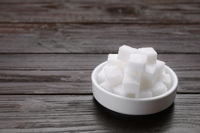 Photo of White sugar cubes on wooden table, space for text