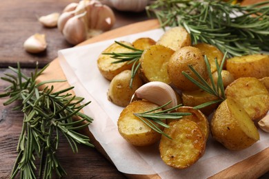 Photo of Delicious baked potatoes with rosemary and garlic on parchment paper, closeup