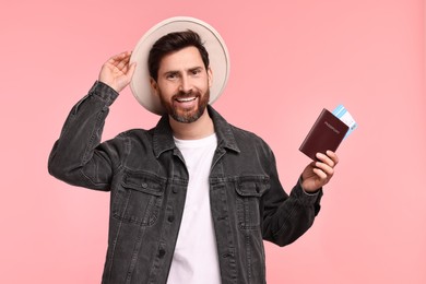 Smiling man with passport and tickets on pink background