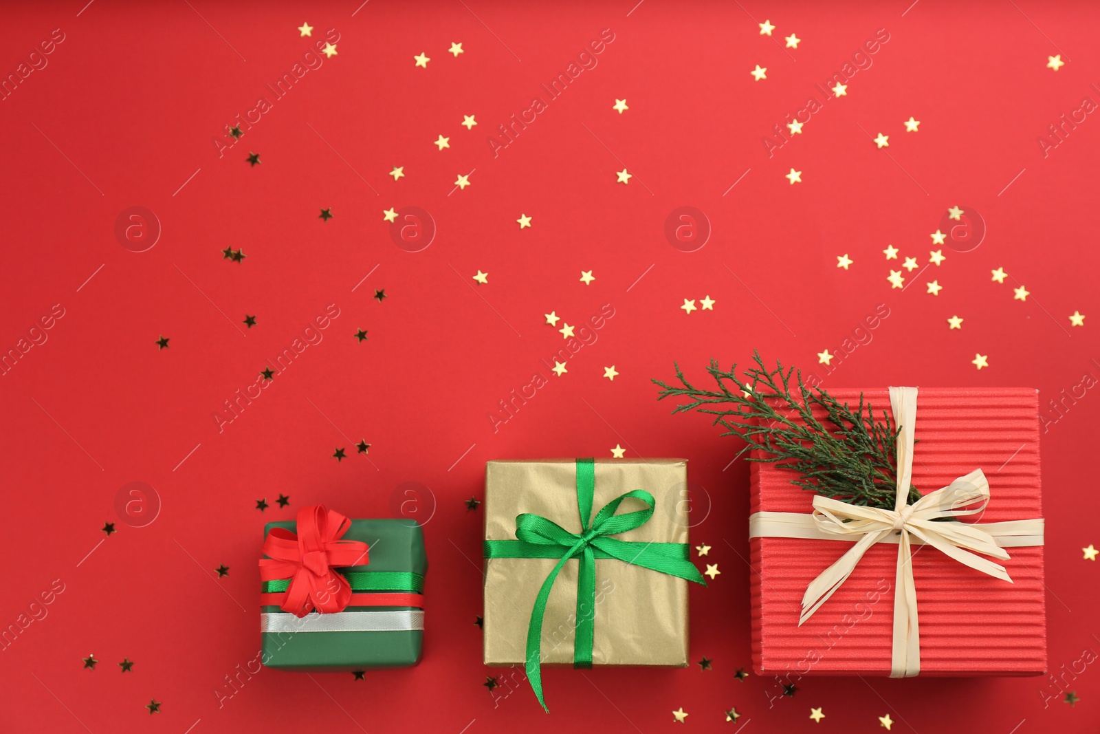 Photo of Christmas gift boxes and shiny confetti on red background, flat lay. Space for text