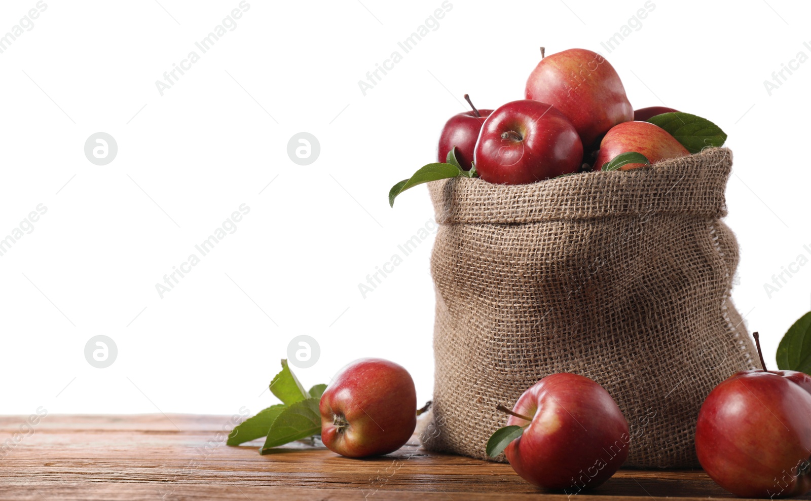 Photo of Ripe red apples with leaves in sack on wooden table against white background. Space for text