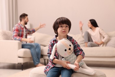 Photo of Sad little boy with toy and his arguing parents on sofa in living room
