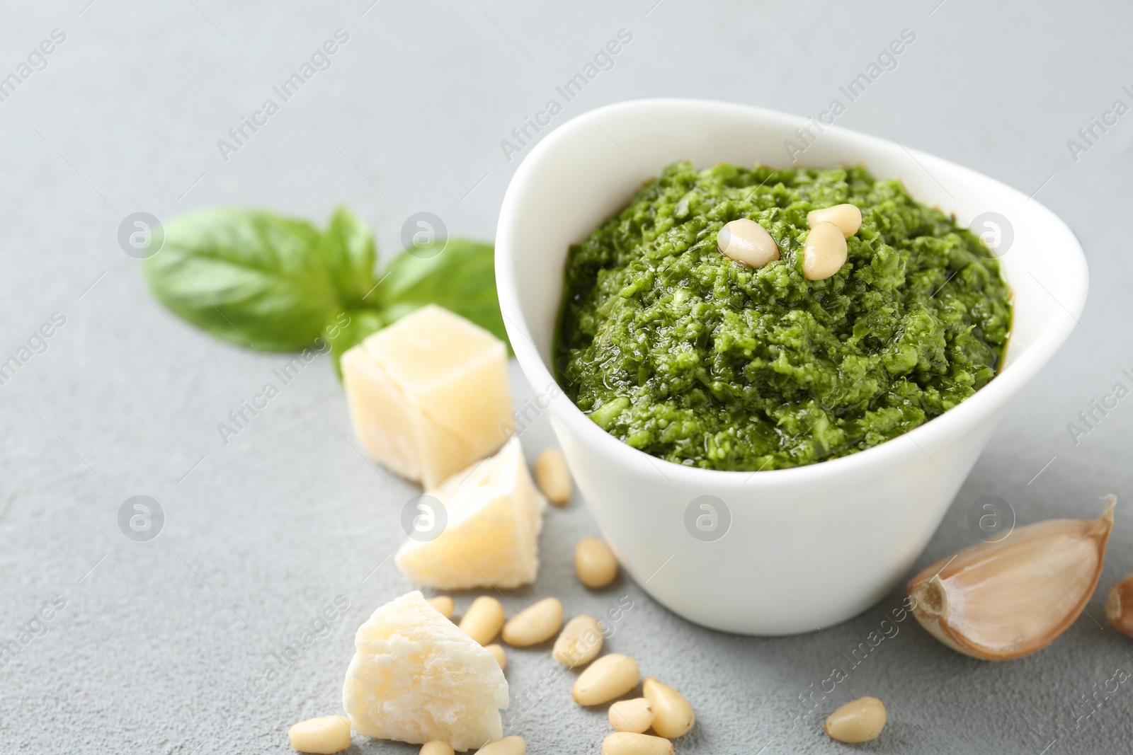 Photo of Composition with bowl of tasty pesto sauce on grey table. Space for text