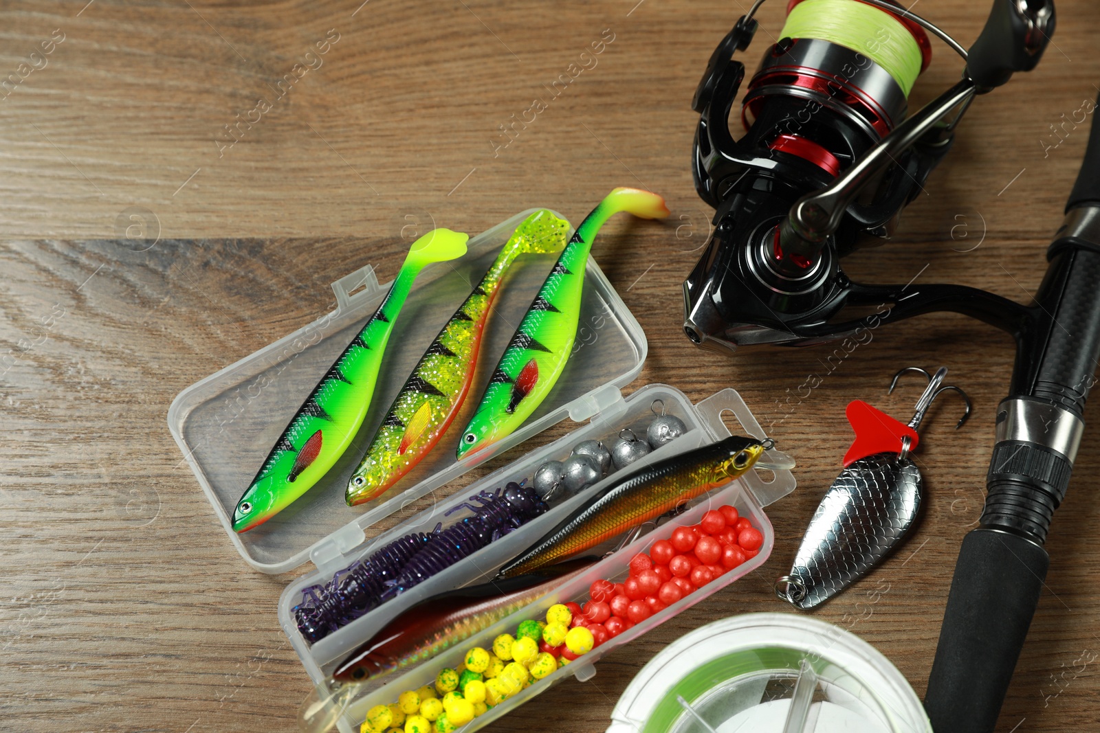 Photo of Fishing rod with spinning reel and baits on wooden background, above view