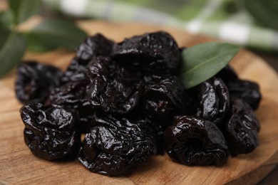 Photo of Tasty dried prunes and green leaf on wooden board, closeup