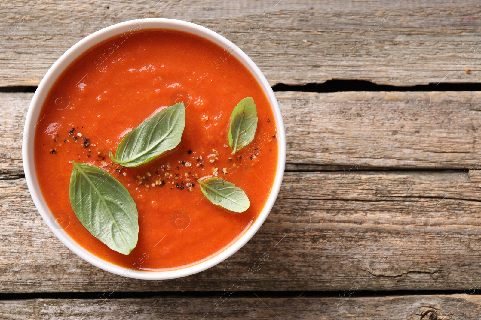 Photo of Delicious tomato soup with basil and spices on wooden table, top view. Space for text