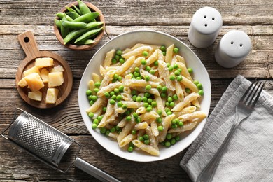 Photo of Delicious pasta with green peas, cheese, grater and fork on wooden table, top view