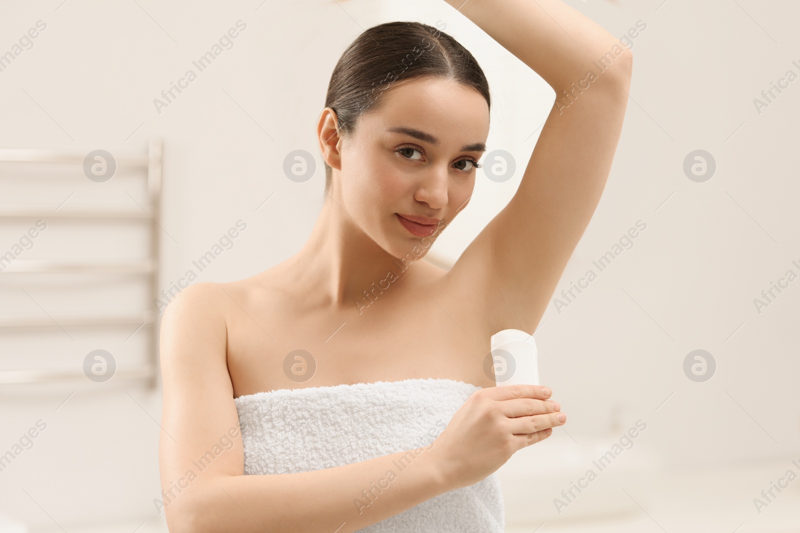 Photo of Beautiful young woman applying deodorant in bathroom