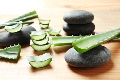 Photo of Fresh aloe vera leaves and spa stones on wooden table