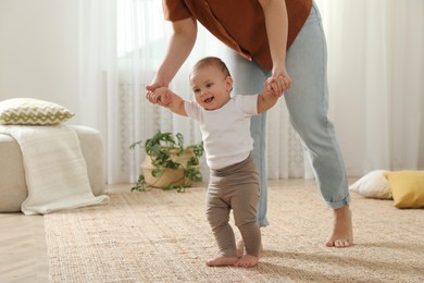 Photo of Mother supporting her baby daughter while she learning to walk at home