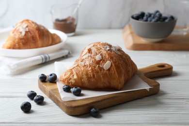 Delicious croissant with almond flakes and blueberries on white wooden table, closeup