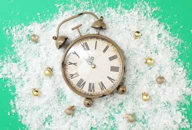 Photo of Alarm clock and festive decor in pile of snow on green background, flat lay. New Year countdown